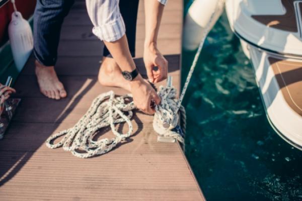 Man standing barefoot on a dock tying up his boat with rope to a dock cleat